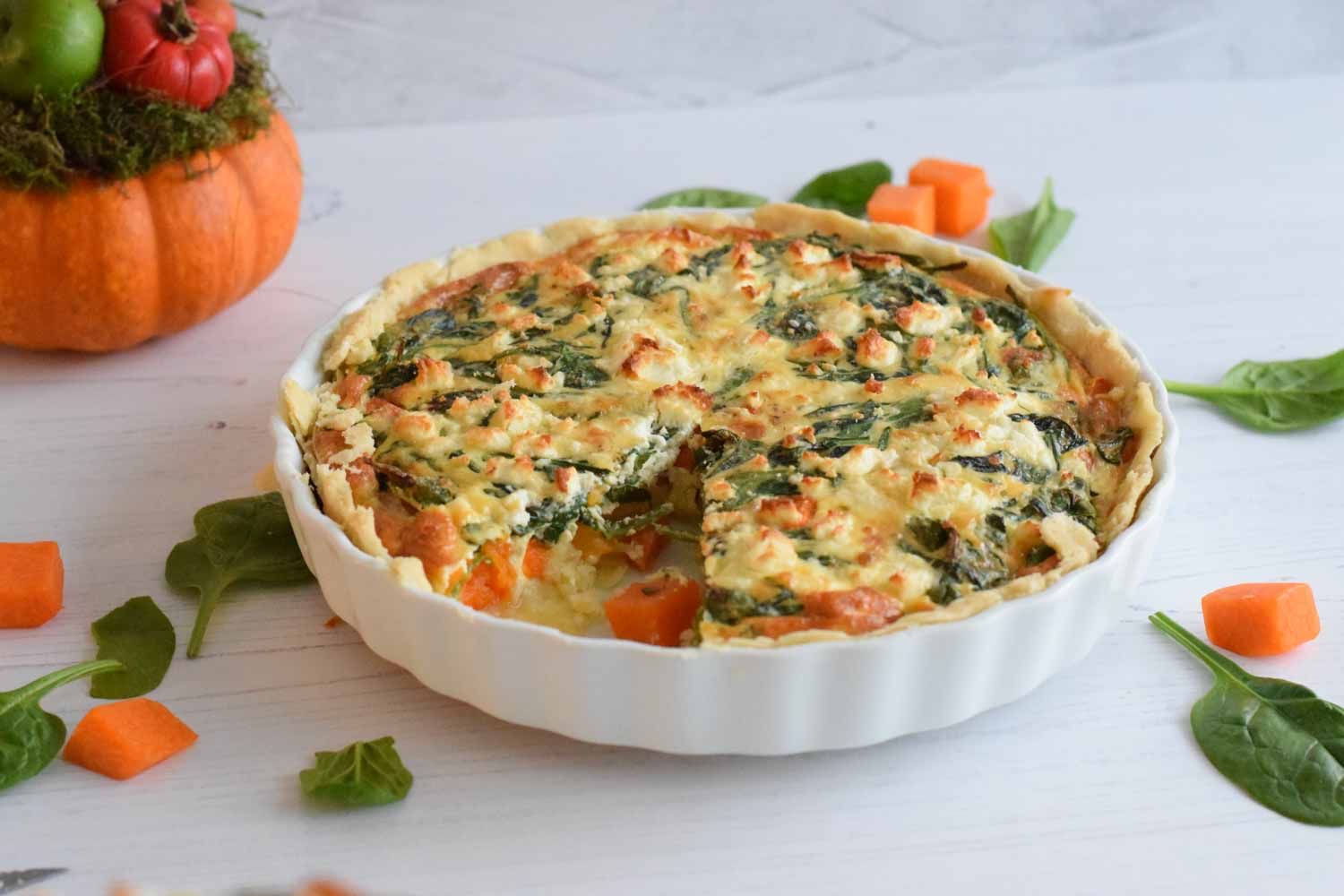A low FODMAP pumpkin and spinach quiche with a decorative pumpkin behind it