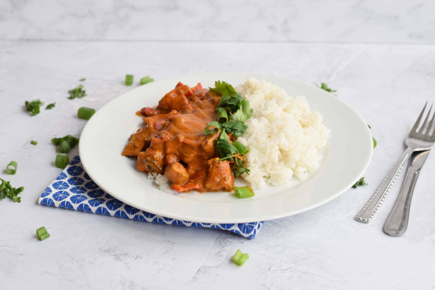 Low FODMAP chicken tikka masala with rice on a plate with cutlery next to it