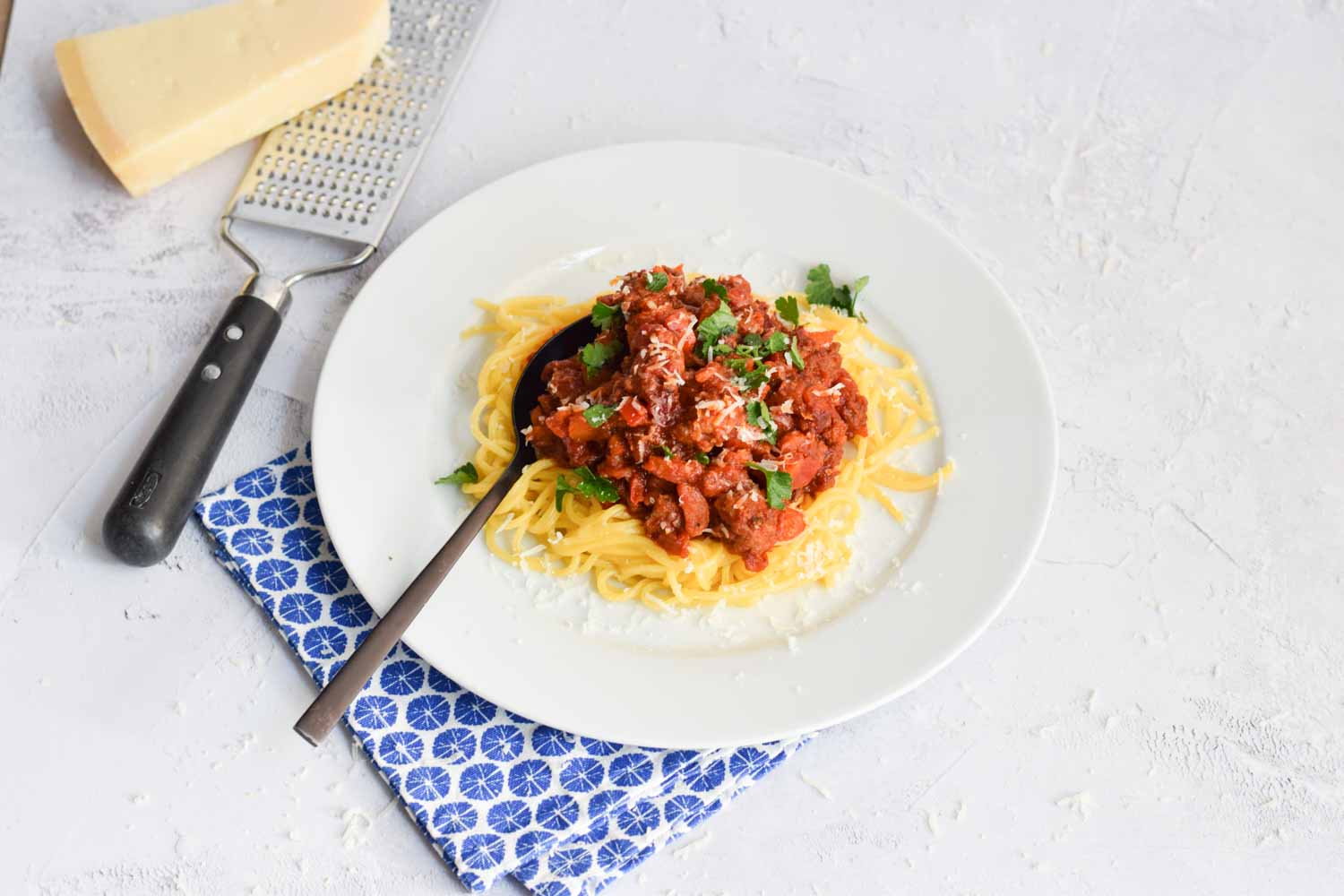 Low FODMAP pasta al ragù on a plate with a piece of parmesan cheese next to it