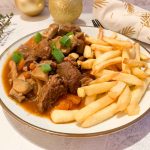 A plate with low FODMAP boeuf bourguignon with spring onion on top and french fries next to it