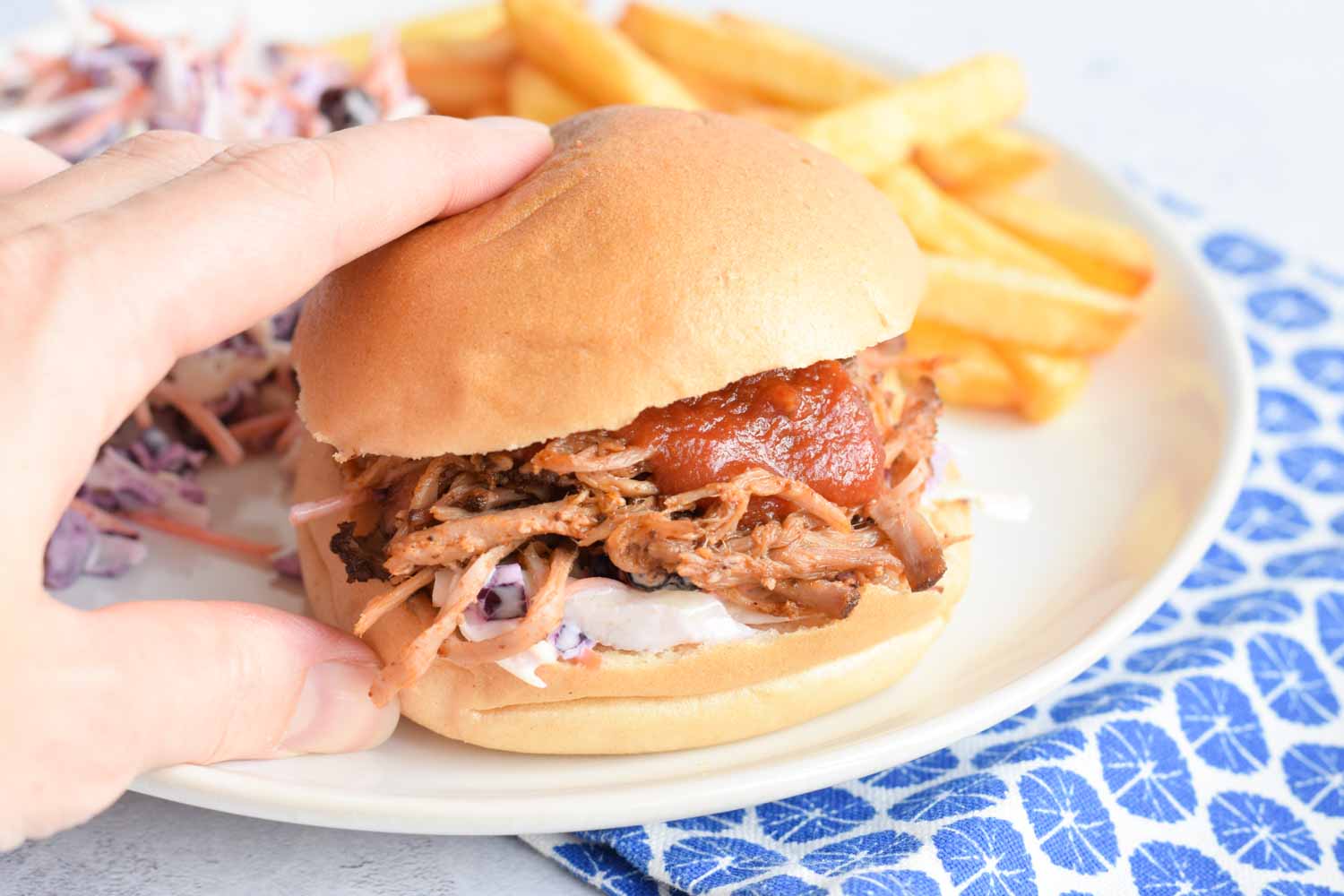 A hand holding a bun with low FODMAP pulled pork and bbq sauce on top of it