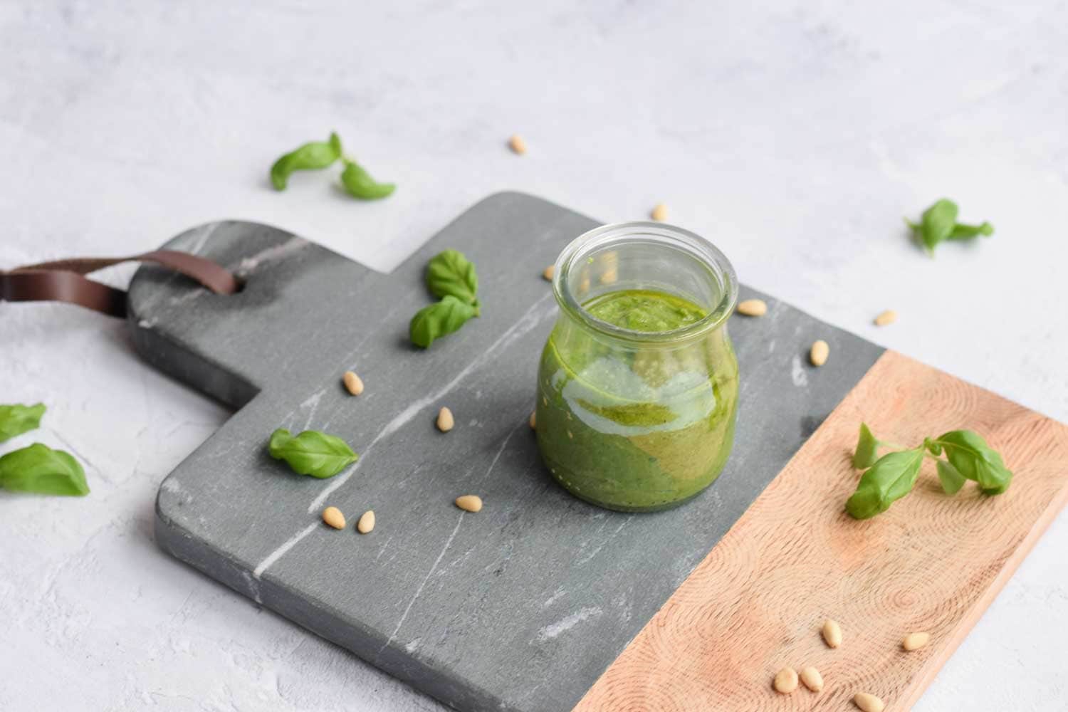 A jar with pesto with pine nuts and basil leaves around