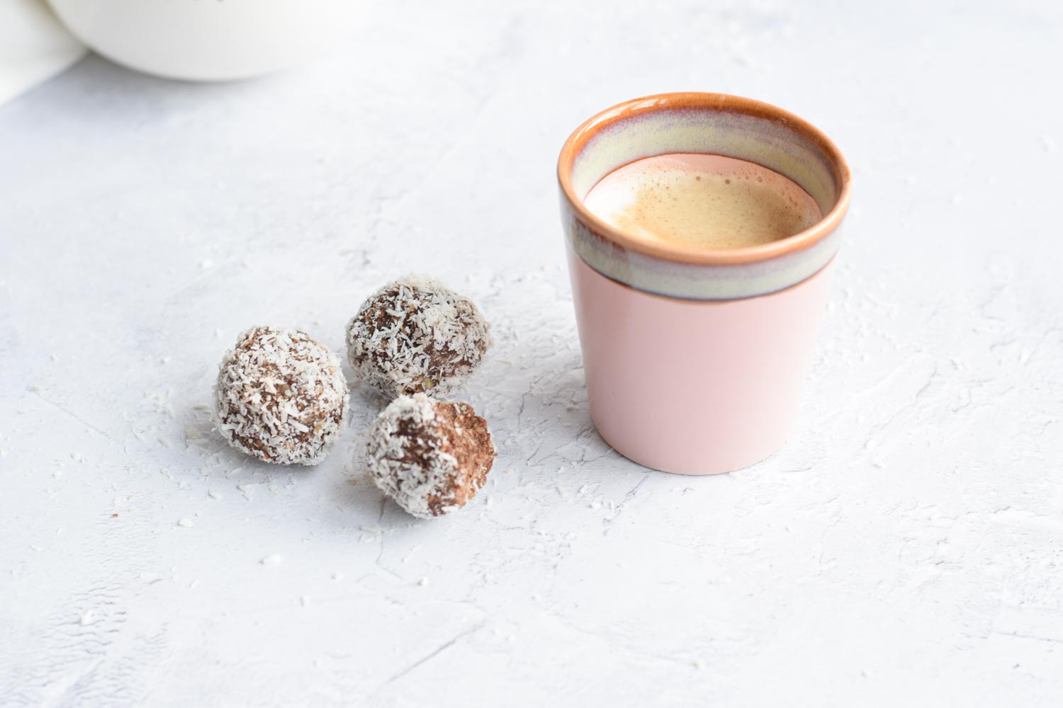 Three chocolate coconut bliss balls with a cup of coffee