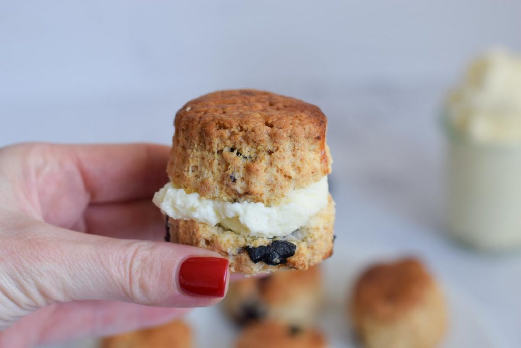 A hand holding a gluten-free blueberry scone with cream