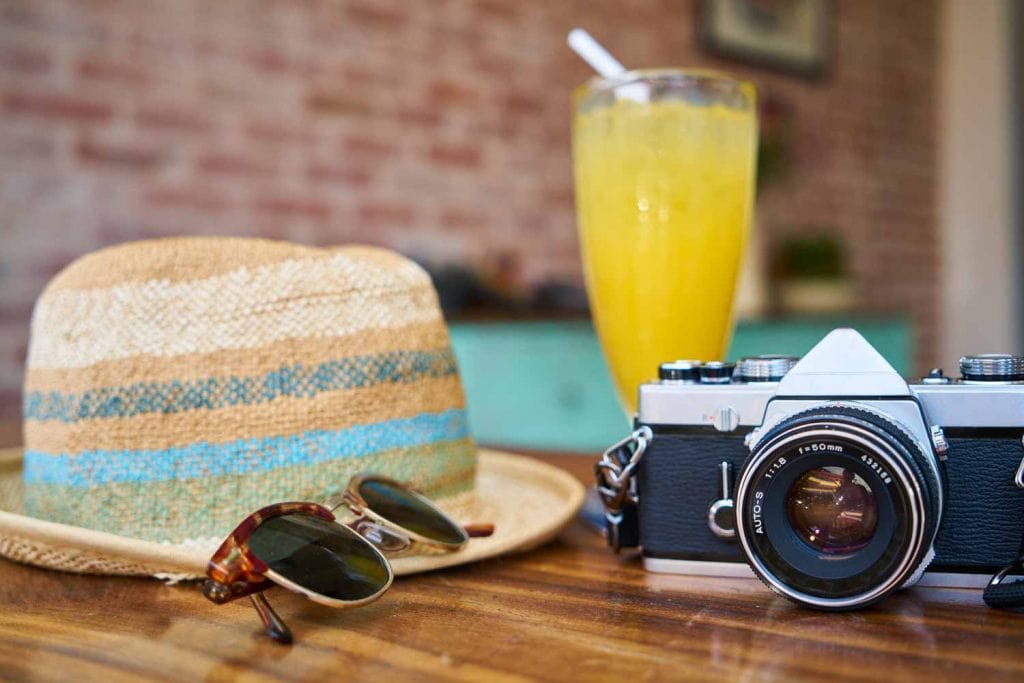 A hat, camera, sunglasses and a glass of juice