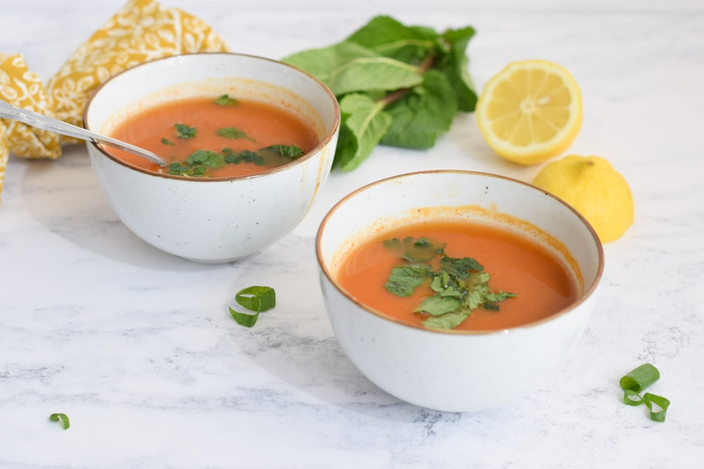 Two bowls of low FODMAP Turkish lentil soup with fresh mint and lemon next to it