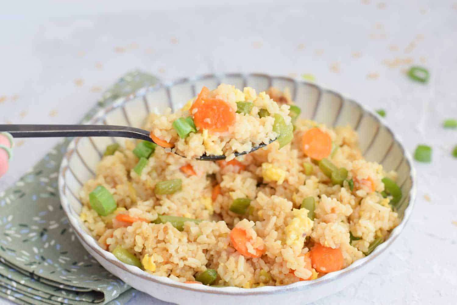 A bowl of low FODMAP fried rice with a spoon above it taking a spoonful out of it