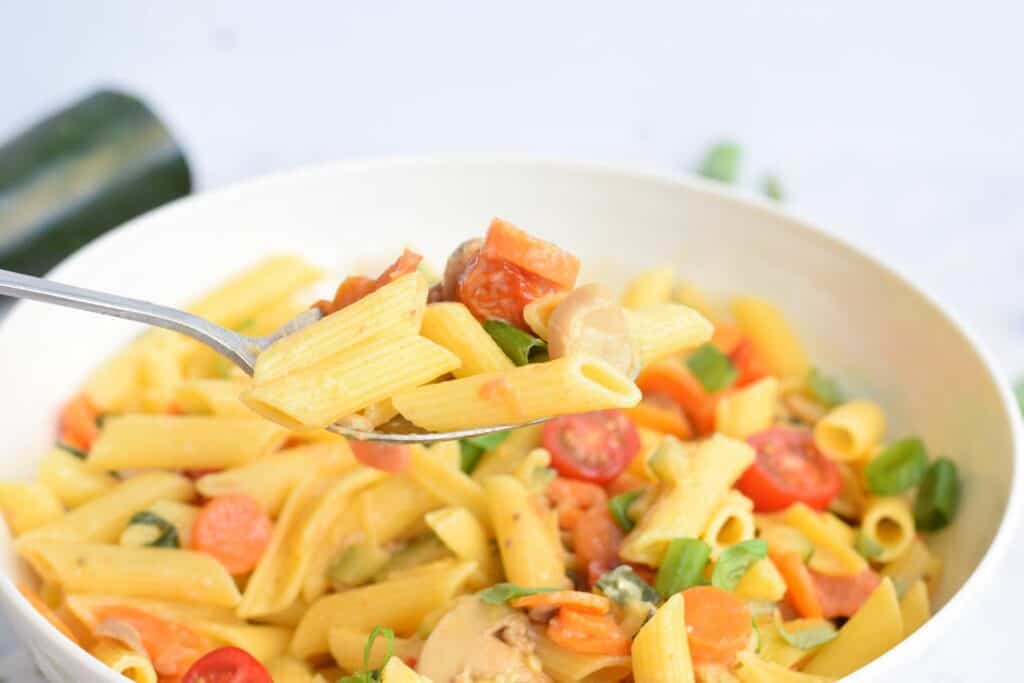 A bowl low FODMAP pasta primavera with a spoon holding a bite
