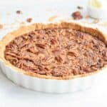 A low FODMAP pecan pie in a pie tin with pecans sprinkled around