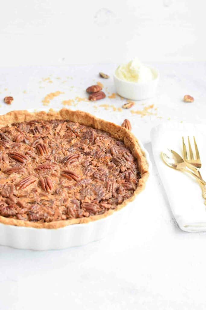 A pecan pie with a white napkin and golden cutlery next to it