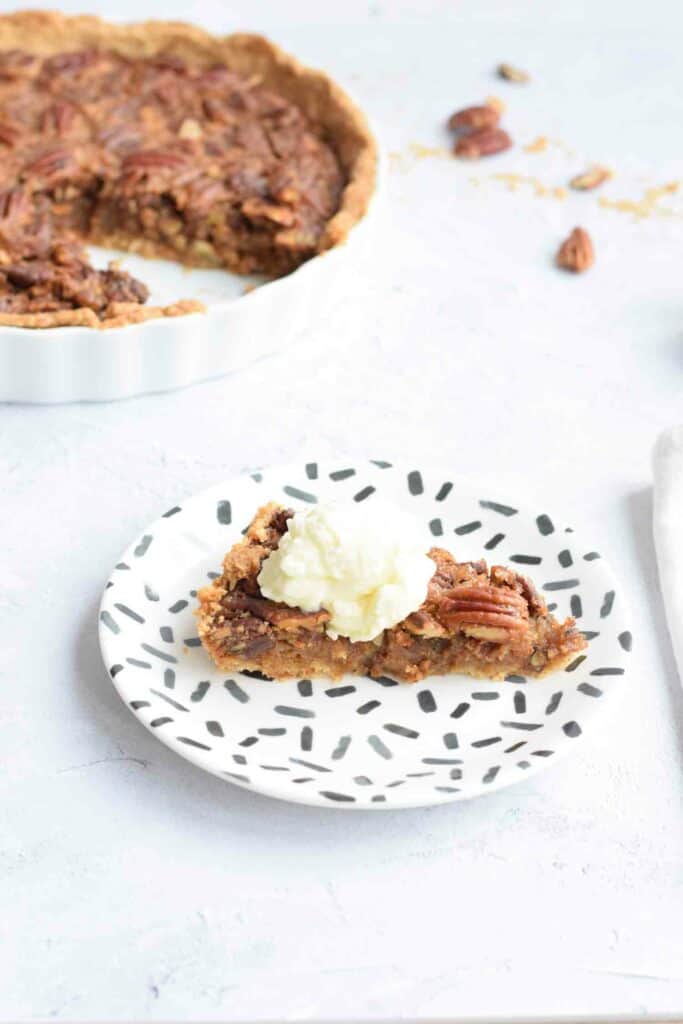 A piece of low FODMAP pecan pie on a plate with a dollop of cream on top