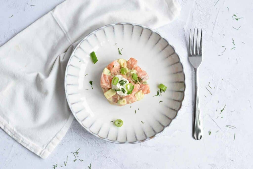 Low FODMAP salmon tartare on a plate with a fork and napkin next to it. Photographed from above. 