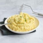 A plate with low FODMAP mashed potatoes with a potato masher behind it