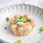 A deep plate with low FODMAP salmon tartare with avocado on it. With spring onion sprinkled on top