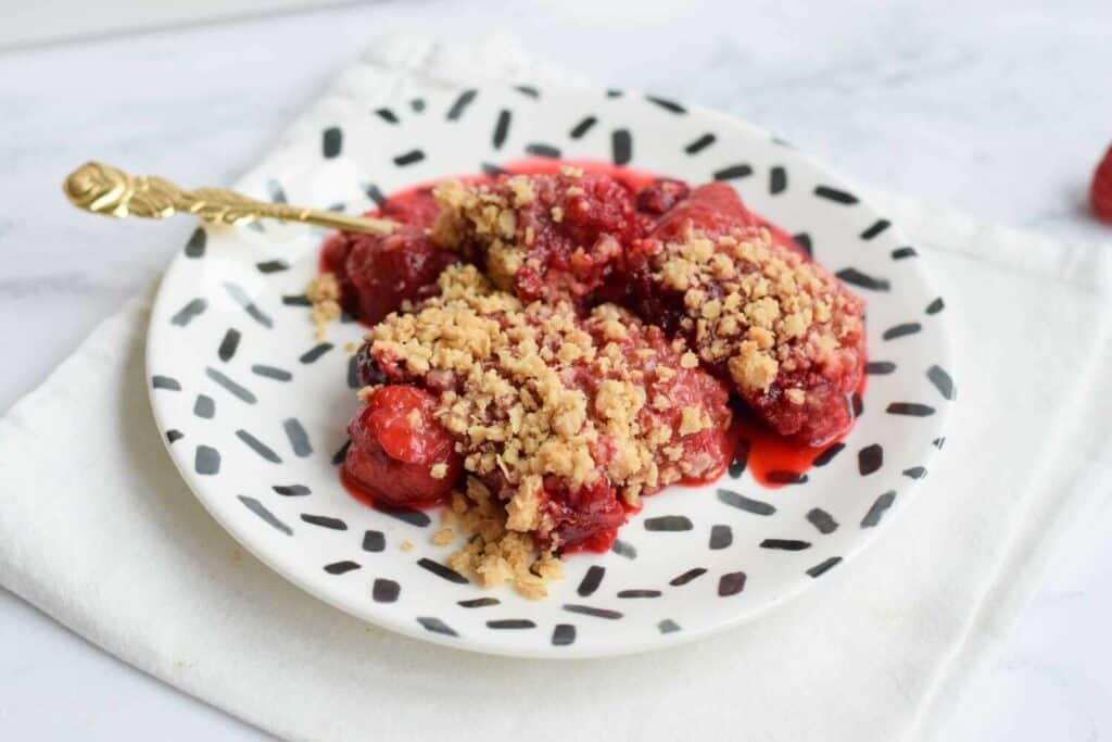A plate with low FODMAP strawberry raspberry crisp with a golden spoon