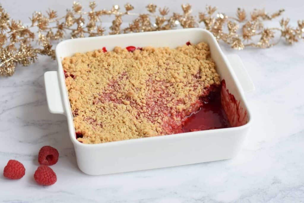 An oven dish with strawberry raspberry crisp and some raspberries in front