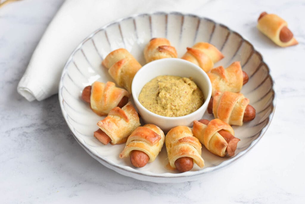 Low FODMAP pigs in a blanket on a plate with some mustard