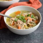 A bowl of low FODMAP chicken soup with a spoon in it