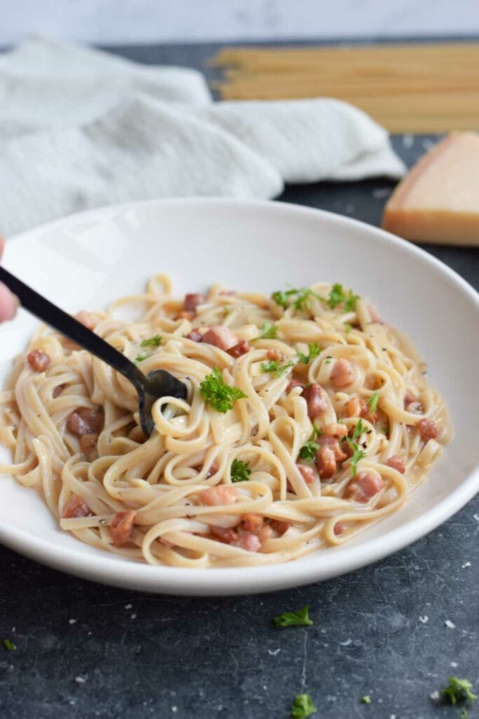 A plate of low FODMAP pasta carbonara with a fork in it