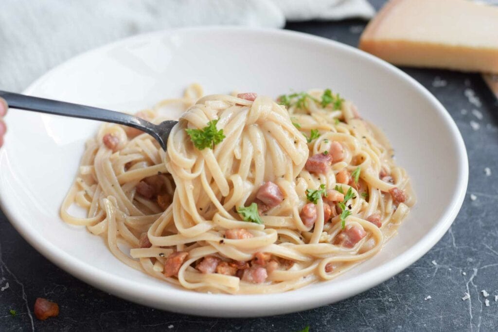 A plate of low FODMAP pasta carbonara where somebody takes a bite out of it