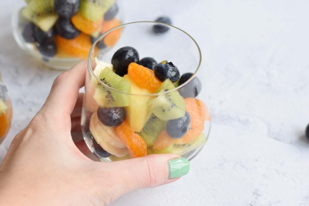 A hand holding a glass with low FODMAP fruit salad