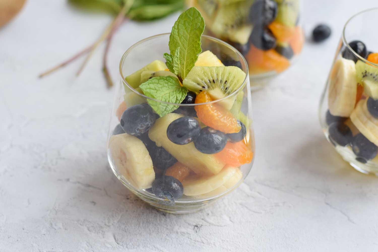 A glass of low FODMAP fruit salad with some mint on top