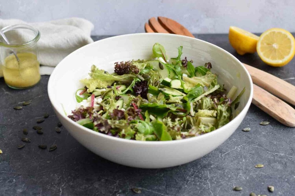 Low FODMAP green salad in a bowl with wooden spoons next to it