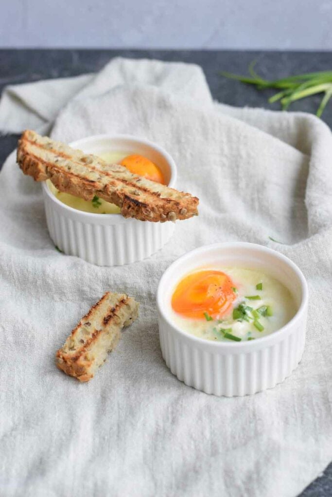 Two bowls of baked eggs with bread next to it