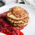 A stack of low FODMAP banana egg pancakes on a plate with red fruits
