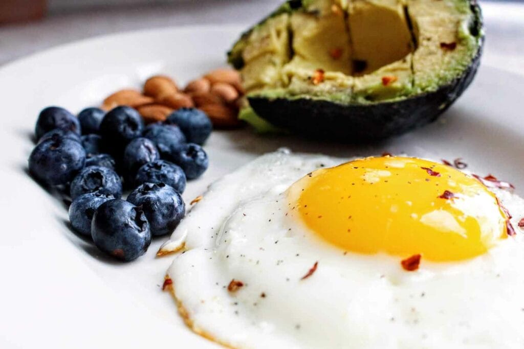 A plate with a fried egg, blueberries and some avocado on it