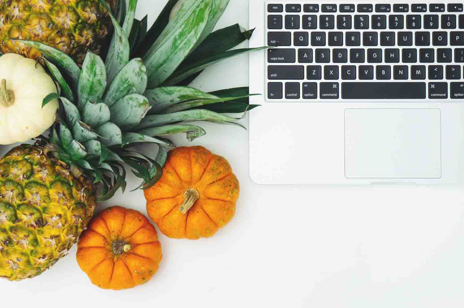 A laptop with pumpkins and a pineapple next to it