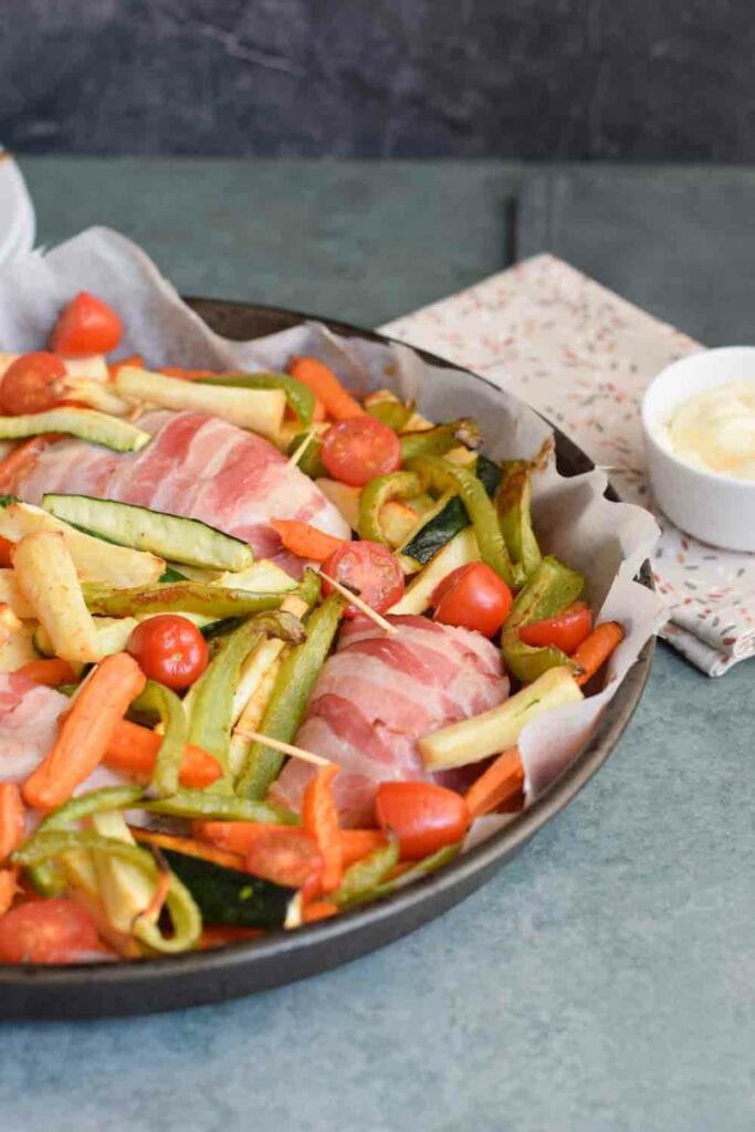 Een low FODMAP traybake met kip in spek en groenten met een bakje mayonaise ernaast