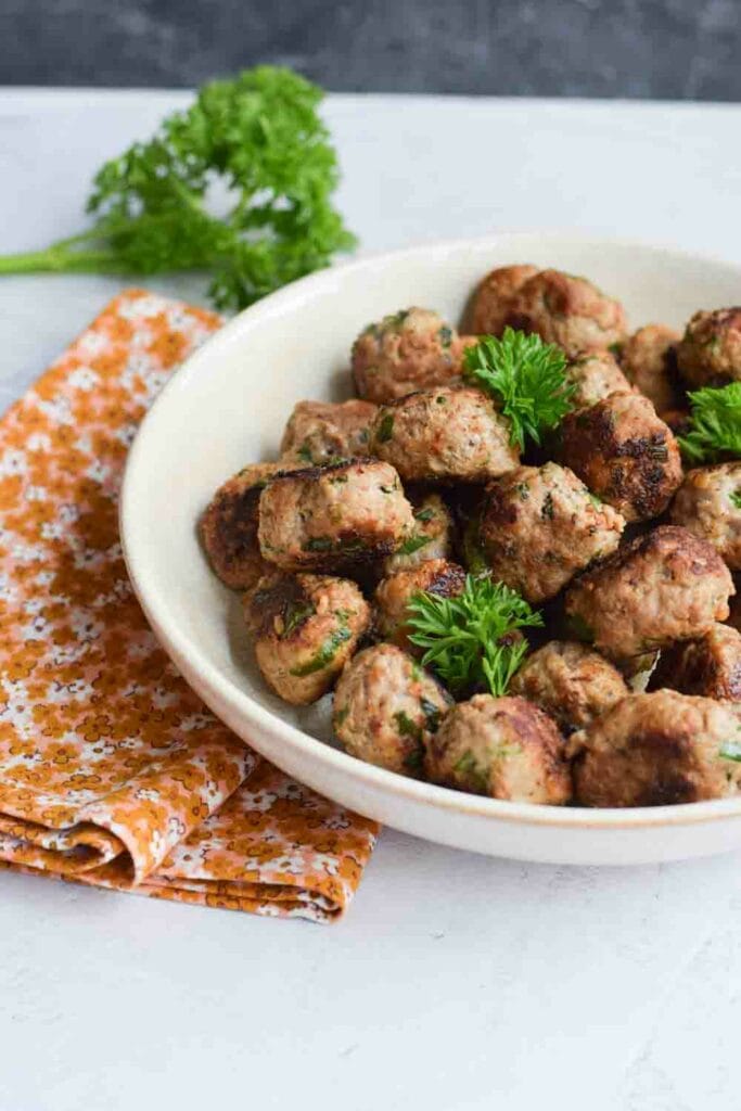 A plate with low FODMAP meatballs with an orange napkin next to it