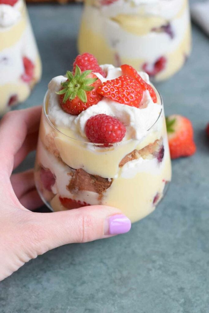 Somebody holding a glass with a low FODMAP trifle with strawberries and raspberries