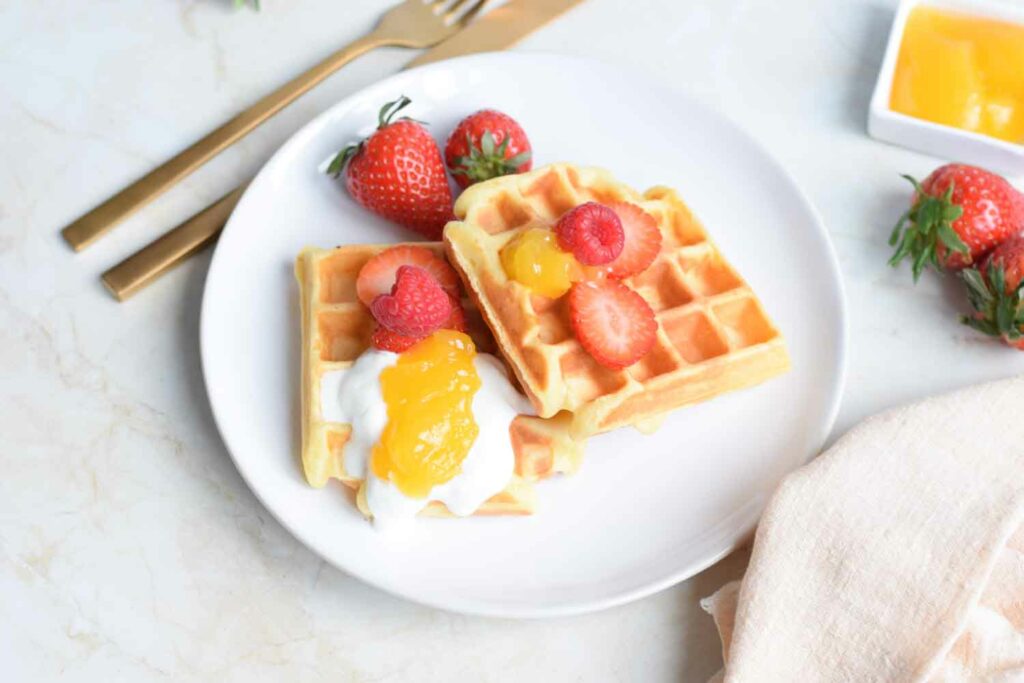 Two low FODMAP waffles on a plate with strawberries, lemon curd and yogurt