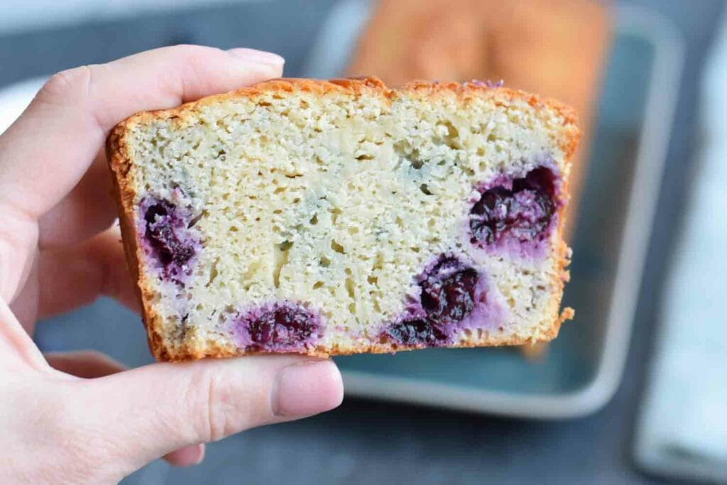 Somebody holding a piece of gluten-free yogurt cake with blueberries