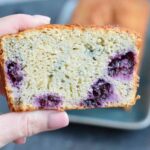 Somebody holding a piece of gluten-free yogurt cake with blueberries